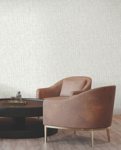 Two brown armchairs with gold legs sit by a round black coffee table topped with a glass bottle and tray, set against York Wallcoverings’ Rian Linear Abstract Wallpaper and a wooden floor.