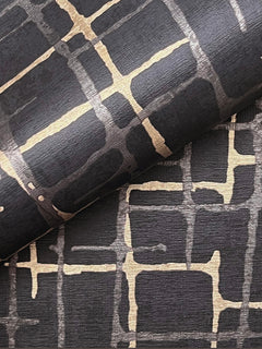 A close-up of two sheets of York Wallcoverings’ Rian Linear Abstract Wallpaper, featuring a black background with an abstract gold grid pattern and textured finish, with one sheet partially rolled over the other.