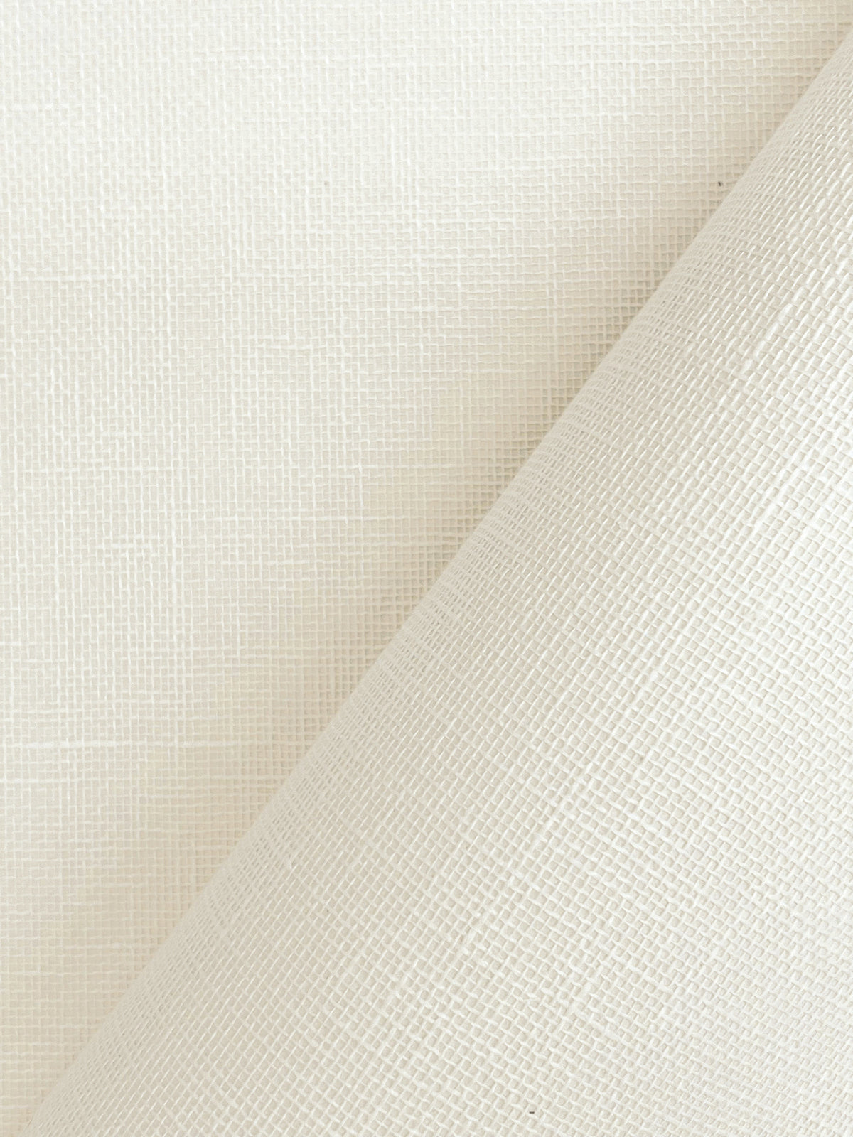 A close-up of York Wallcoverings’ Woven Linen Wallpaper in off-white, featuring a subtle grid texture. One corner is partially peeled back, revealing the matching textured surface beneath.