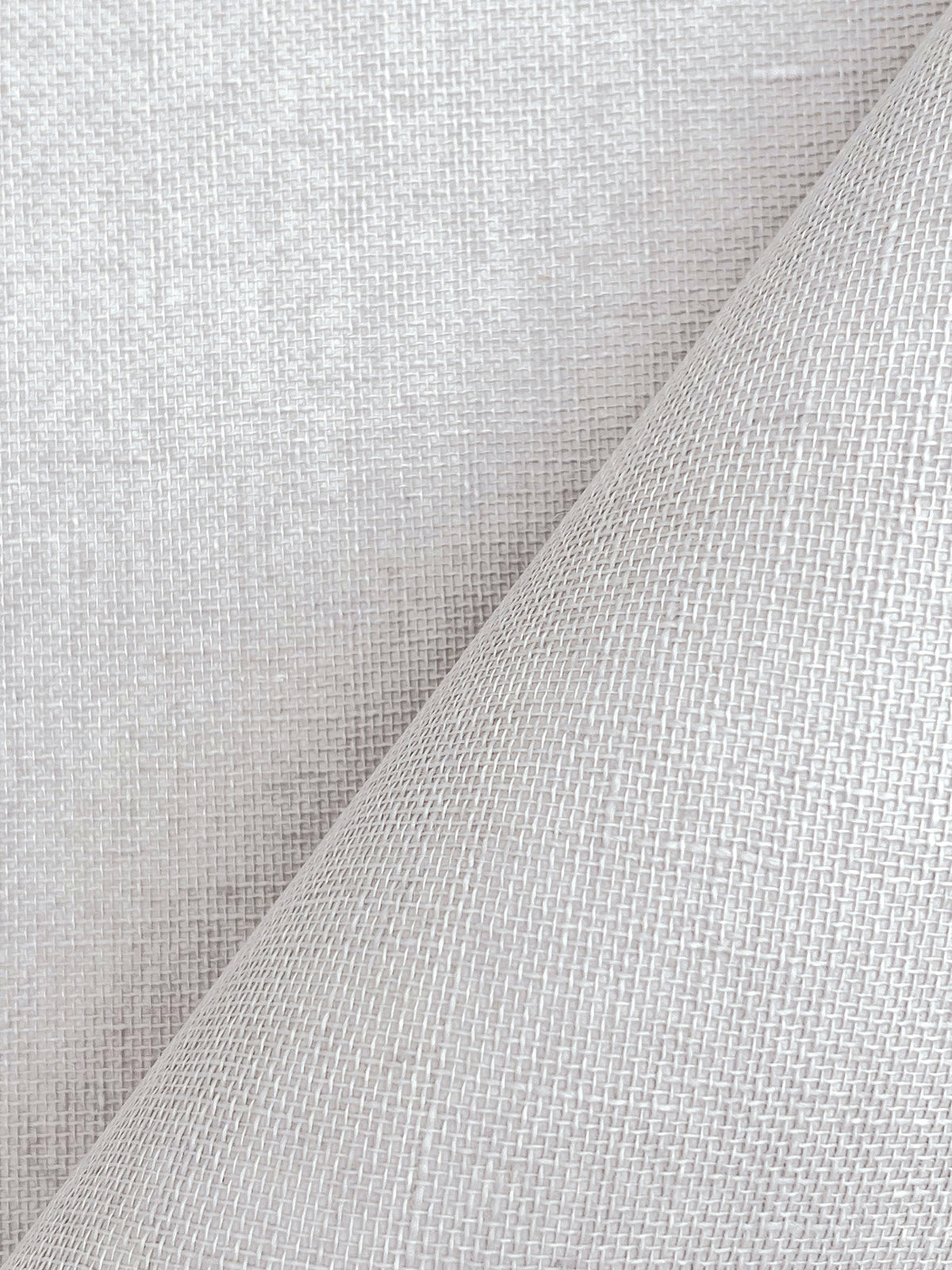 A close-up of York Wallcoverings’ Woven Linen Wallpaper showcases its textured white surface, featuring a diagonal fold that highlights the intricate woven pattern and creates subtle shadows for added depth.