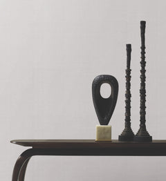 Minimalist scene featuring two tall, dark sculptural objects and an abstract oval-shaped sculpture arranged on a small table, set against a plain background covered in Woven Linen Wallpaper by York Wallcoverings.