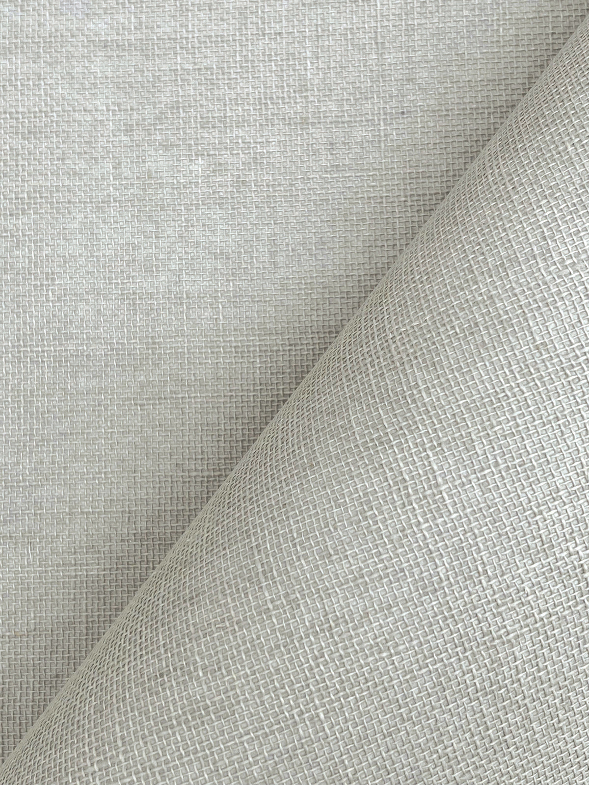 Close-up of Woven Linen Wallpaper by York Wallcoverings in light gray, featuring a textured, grid-like pattern. One section is rolled diagonally across the image, highlighting the intricate weave and subtle sheen of the wallpaper.