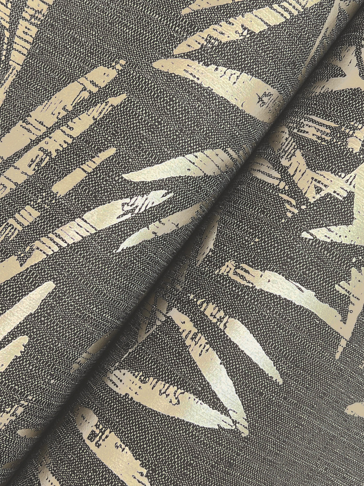 Close-up of the Allerton Bamboo Wallpaper, showcasing its textured surface with a black and gold abstract leaf pattern. Diagonal, metallic gold shapes stand out against a dark background, with a slight fold visible at the center.