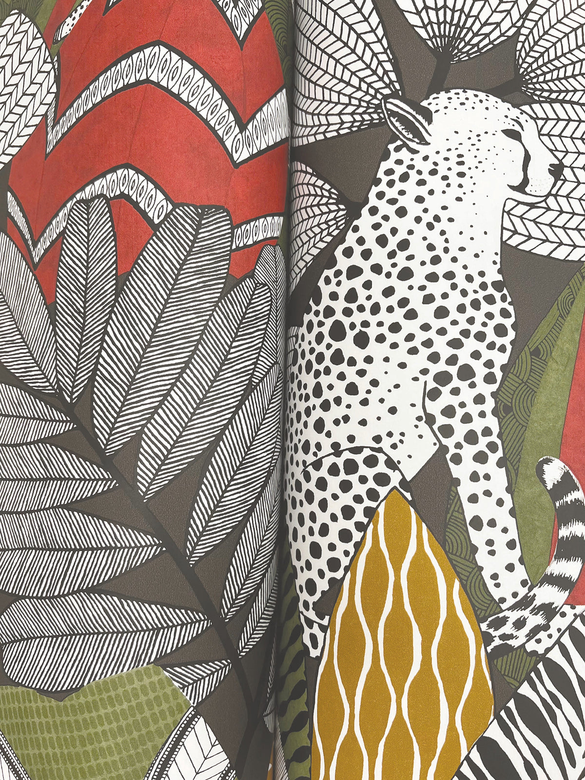 The Namiri Wallpaper by York Wallcoverings features an illustrated cheetah with black spots sitting among large, stylized leaves in shades of green, red, white, and yellow, creating a bold, patterned, jungle-inspired design.