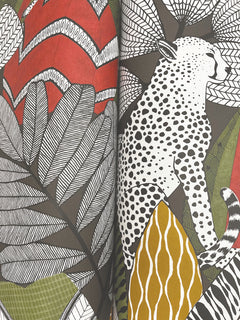 Namiri Wallpaper by York Wallcoverings features an illustrated cheetah with black and white spots, surrounded by bold, patterned leaves in vibrant red, green, yellow, and gray hues.