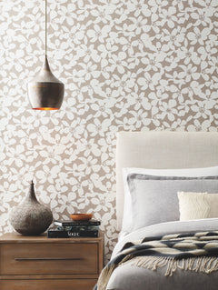 A modern bedroom featuring the Free Spirit Wallpaper by York Wallcoverings, a beige upholstered bed, gray and white bedding, a wooden nightstand with books, a decorative vase, and a metallic pendant light.