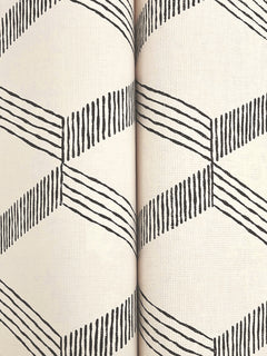 Close-up of two rolls of Palisades Paperweave Wallpaper by York Wallcoverings, featuring a cream background and a repeating black geometric zigzag pattern made from angled lines.