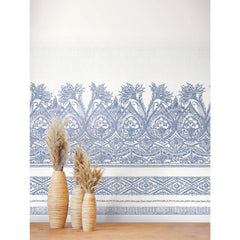 Three woven vases filled with dried grasses sit on a wooden surface in front of a wall adorned with the Henna Wall Mural by York Wallcoverings, featuring intricate blue and white floral and geometric patterns.
