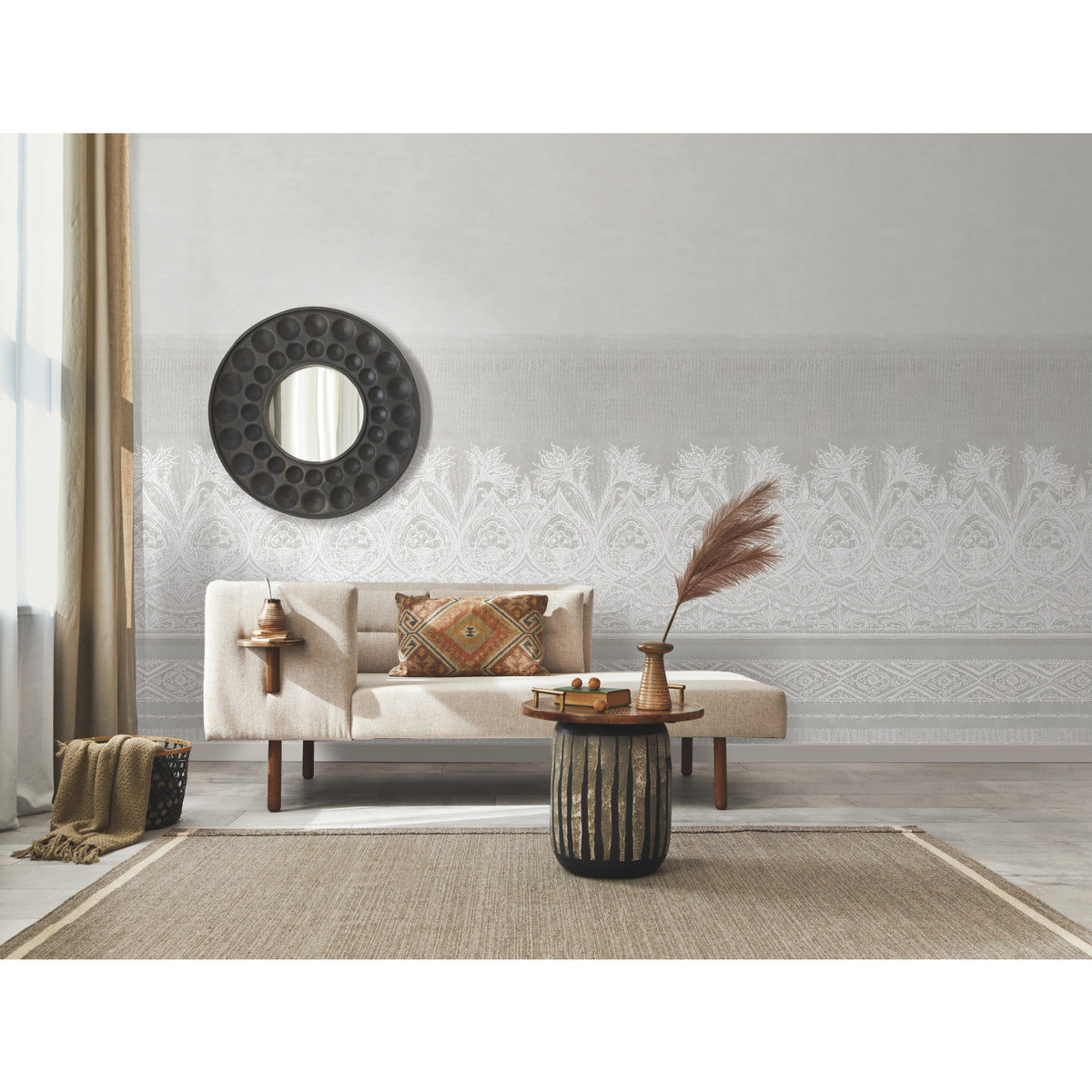A modern living room featuring the Henna Wall Mural by York Wallcoverings, a beige sofa, a round black mirror on the wall, a woven rug, and a small coffee table adorned with dried pampas grass and decor. Light streams in from a window dressed with beige curtains.