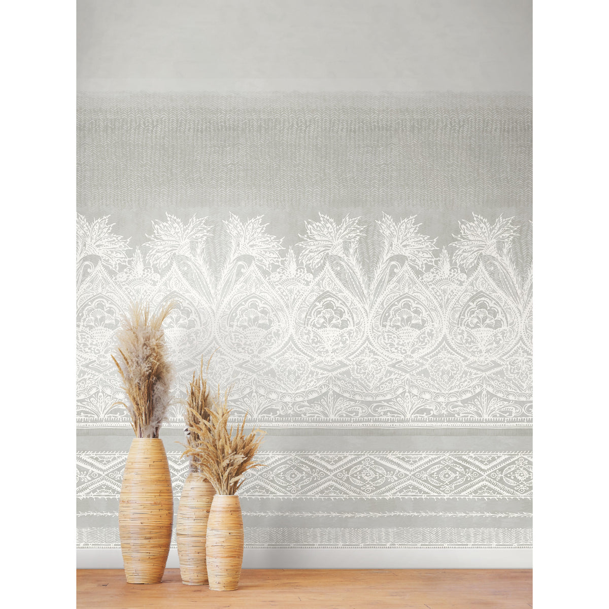 Three tall vases with dried grasses stand on a wooden floor in front of a light gray wall adorned with the Henna Wall Mural by York Wallcoverings, featuring an intricate white floral and geometric pattern.