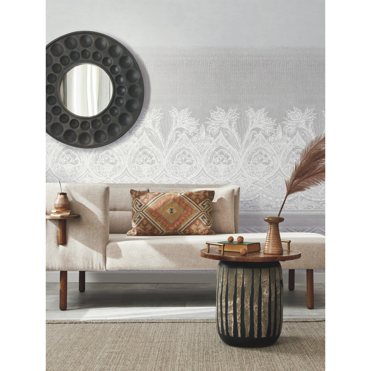 Modern living room with a beige sofa, patterned pillow, round mirror, side table, vase with dried reeds, decorative tray with fruit, and a textured wall featuring the ornate white Henna Wall Mural by York Wallcoverings.