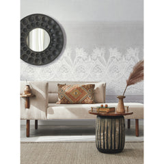 Modern living room with a beige sofa, patterned pillow, round mirror, side table, vase with dried reeds, decorative tray with fruit, and a textured wall featuring the ornate white Henna Wall Mural by York Wallcoverings.