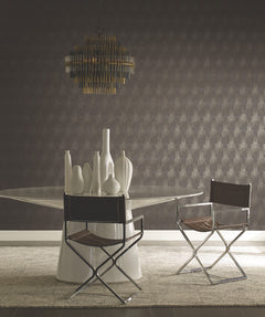 Modern dining area with a round glass table, white ceramic vases, two metal-framed chairs with brown seats, a geometric gold chandelier, and Flapper Wallpaper by York Wallcoverings.