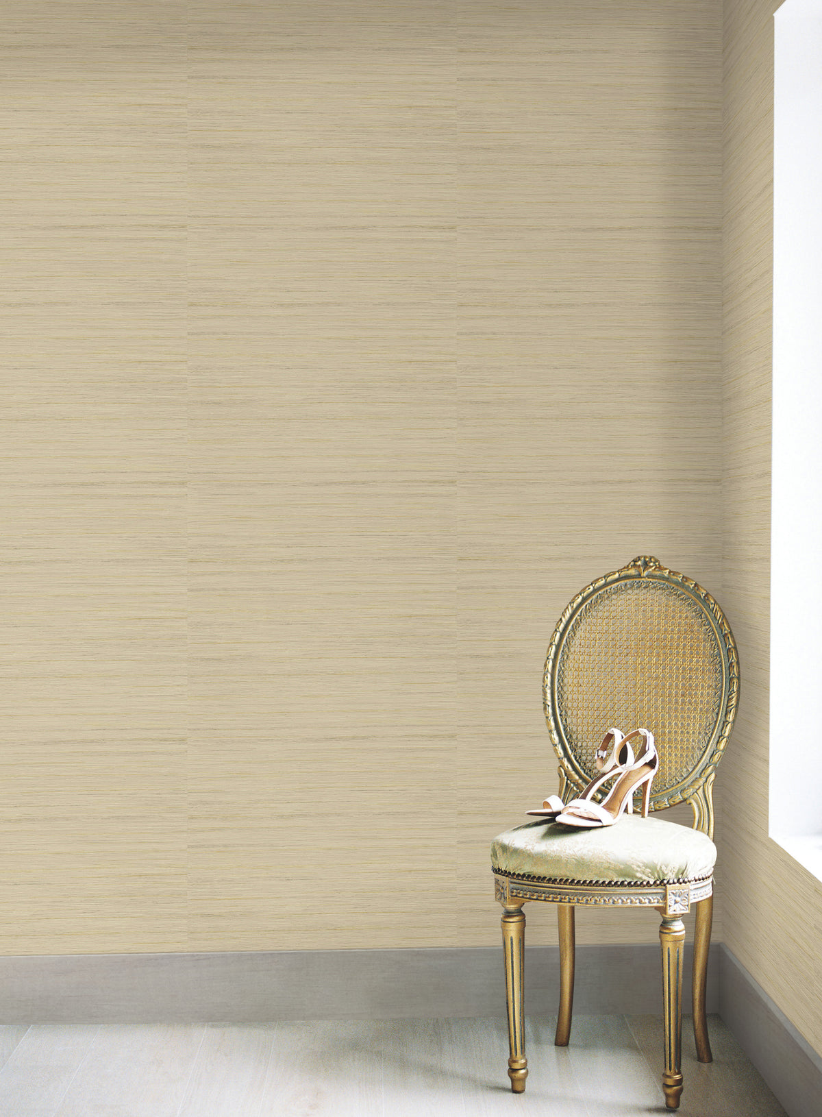 A pair of high-heeled shoes rests on an ornate, gold-trimmed chair by a window in a room featuring York Wallcoverings’ Ragtime Silk Wallpaper and light wood flooring.