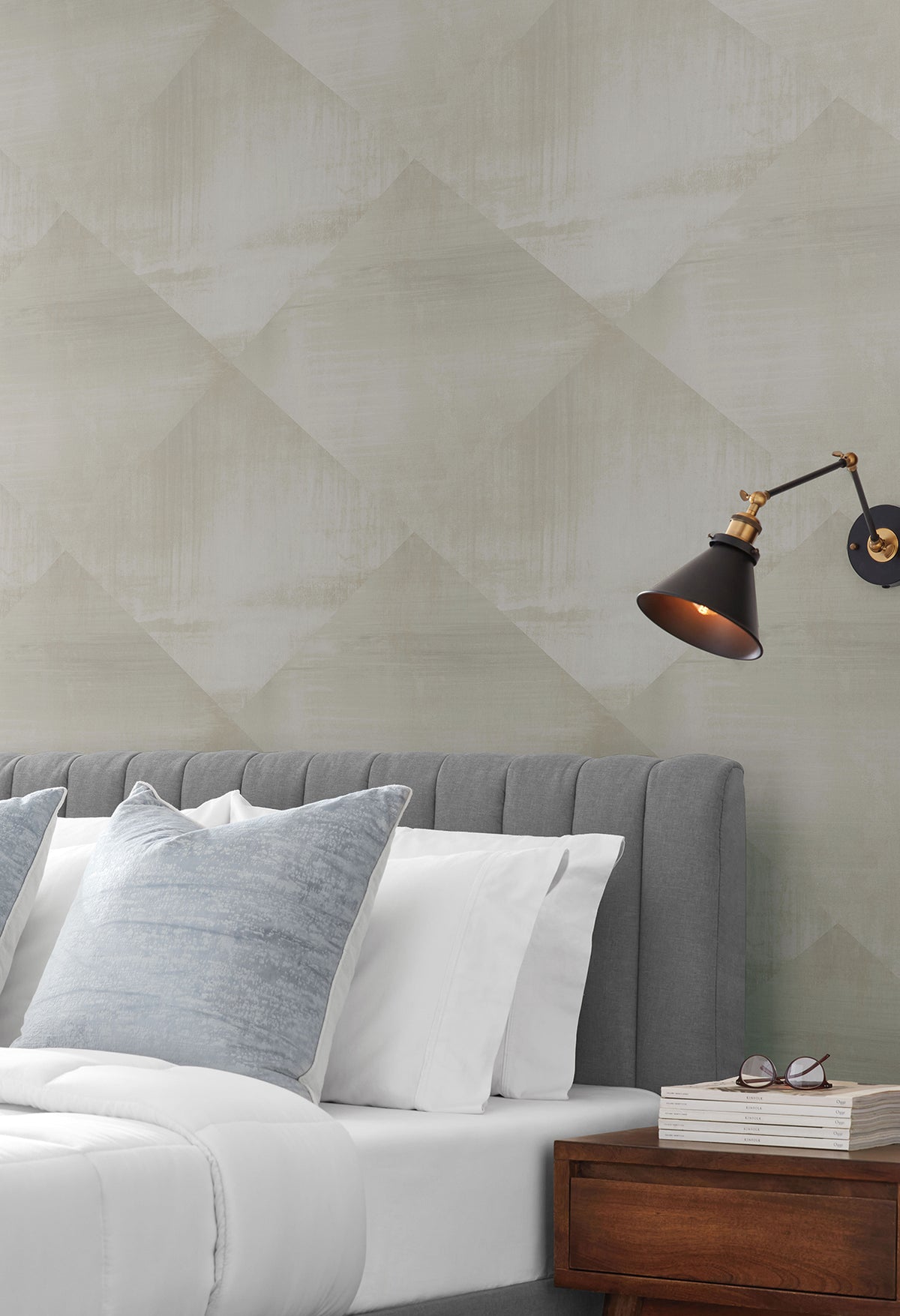 In Clay Wallpaper with a subtle, geometric diamond pattern in shades of light gray, installed in a bedroom behind a gray tufted headboard.