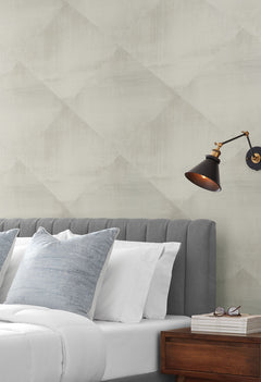 In Clay Wallpaper with a subtle, large-scale diamond pattern behind a bed with a gray tufted headboard and a black wall-mounted lamp.