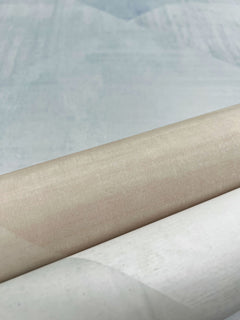 A roll of In Clay Wallpaper featuring a smooth, light beige surface layered over a textured pale blue background.