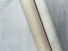 Two rolls of In Clay Wallpaper with a textured, mottled appearance resting on a piece of the same wallpaper.