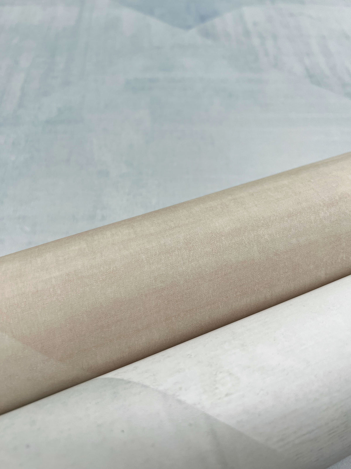 A roll of In Clay Wallpaper featuring a smooth, beige surface transitioning to a textured, light blue area.