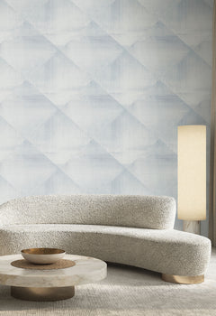 In Clay Wallpaper featuring a pale blue and white geometric diamond pattern behind a curved sofa, round coffee table, and floor lamp.