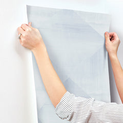 Hands applying a sheet of light blue geometric-patterned In Clay Wallpaper by York Wallcoverings to a wall.