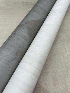 Two rolls of In Clay Wallpaper featuring a subtle, textured geometric pattern in shades of gray and white.