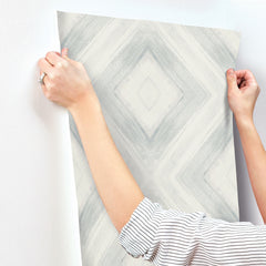 Hands holding a strip of grey and white geometric diamond Ballad Wallpaper against a wall.