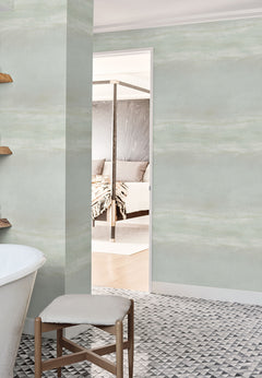Serene Reflection Wallpaper in light green with a subtle, horizontal brushstroke texture installed on walls in a bathroom and bedroom doorway.