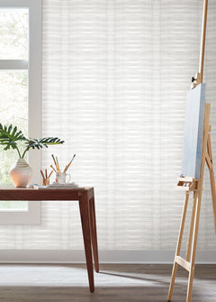 Grey Stone Wallpaper featuring a light grey, horizontal wavy texture covering a wall in a room with a desk and an artist’s easel.
