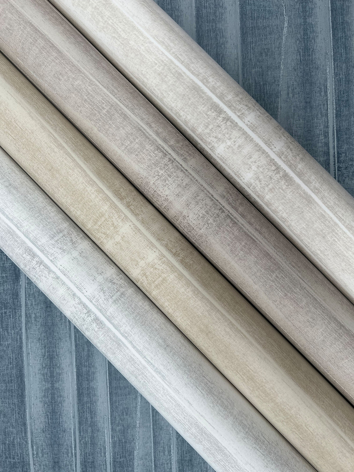 Four rolls of Grey Stone Wallpaper by York Wallcoverings displayed diagonally, showing shades of grey, beige, and white with a subtle textured stone pattern.