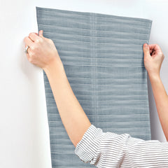 Hands apply a strip of Grey Stone Wallpaper, featuring a horizontal, textured pattern, to a white wall.