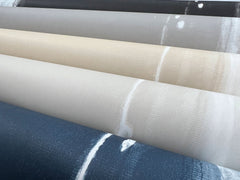 Several rolls of Ink Wash Wallpaper by York Wallcoverings featuring abstract ink wash patterns in blue, beige, grey, and black.