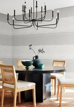 A dining room with a round black table and four chairs set against a wall featuring York Wallcoverings Ink Wash Wallpaper in horizontal grey and white stripes.