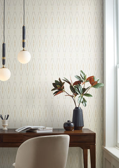 Artifact Silhouettes Wallpaper featuring a repeating pattern of thin, tan diamond shapes on a cream background, installed behind a wooden desk with a plant and pendant lights.