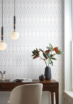 Artifact Silhouettes Wallpaper featuring a repeating pattern of thin, vertical blue and gray diamond shapes on a white background, installed in a home office with a wooden desk and chair.