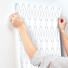 Hands applying a sheet of geometric diamond-patterned Artifact Silhouettes Wallpaper by York Wallcoverings to a white wall.