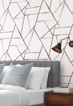 Intersect Wallpaper featuring a geometric pattern of intersecting, distressed mauve lines on a white background, installed behind a gray tufted headboard.
