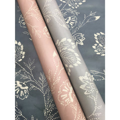 Two rolls of Barbier Wallpaper featuring a dotted floral pattern, one in blush pink and one in grey, resting on a sheet of the same grey floral wallpaper.