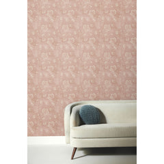 Barbier Wallpaper featuring a white botanical line-art pattern on a dusty pink background, shown on a wall behind a beige curved sofa.