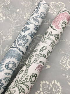 Two rolls of Fontaine Wallpaper with a floral block-print pattern resting on a matching flat sheet of the same design.