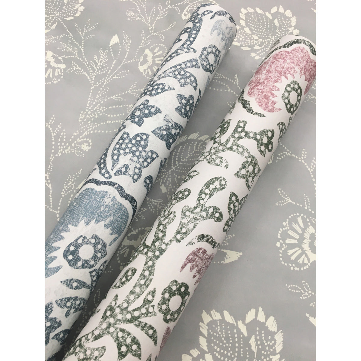 Two rolls of Fontaine Wallpaper featuring a floral pattern, resting against a matching grey floral background.