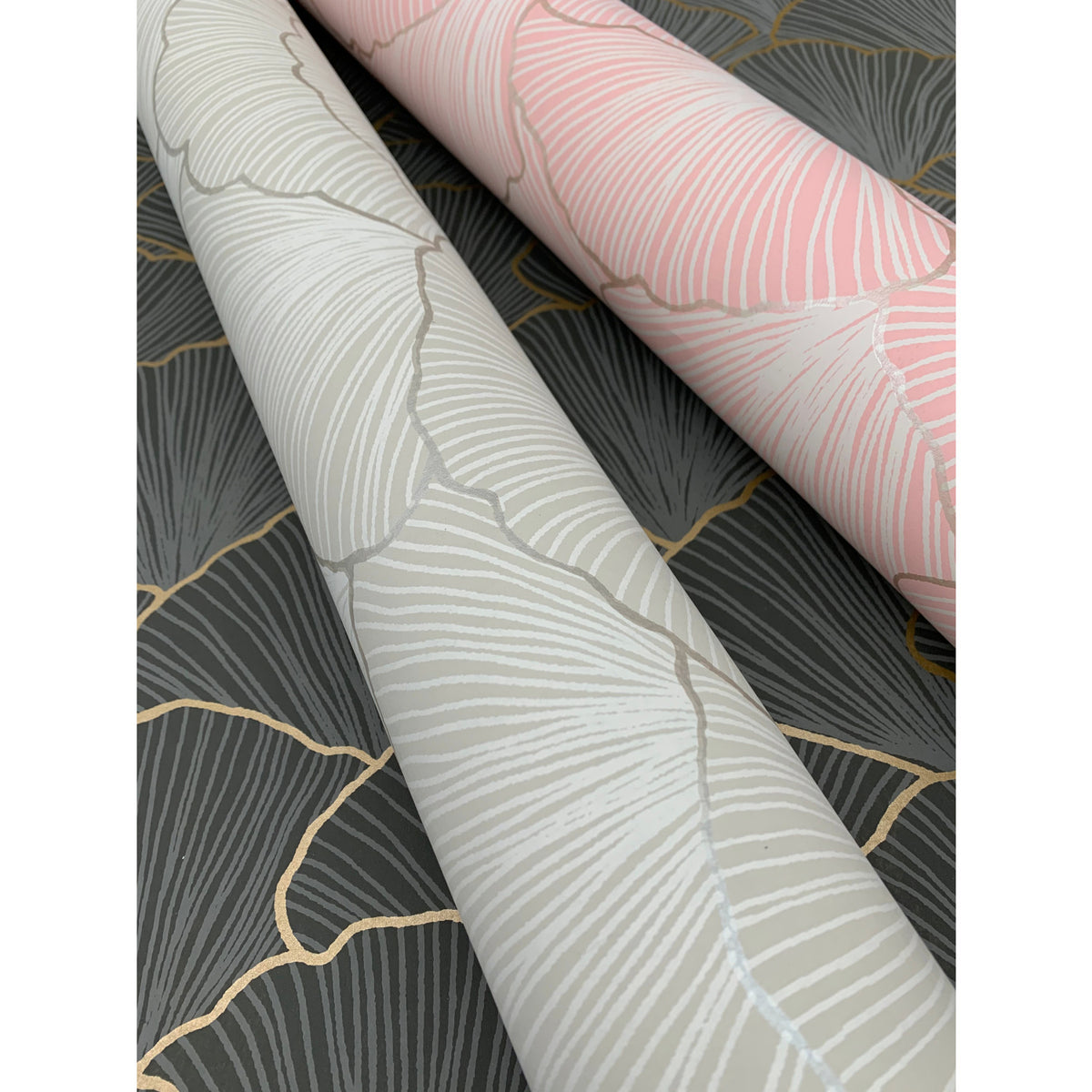 Two rolls of Candice Olson Luminous Gingko Wallpaper featuring a gingko leaf pattern in light gray and light pink, displayed against a dark gray background with gold outlines.