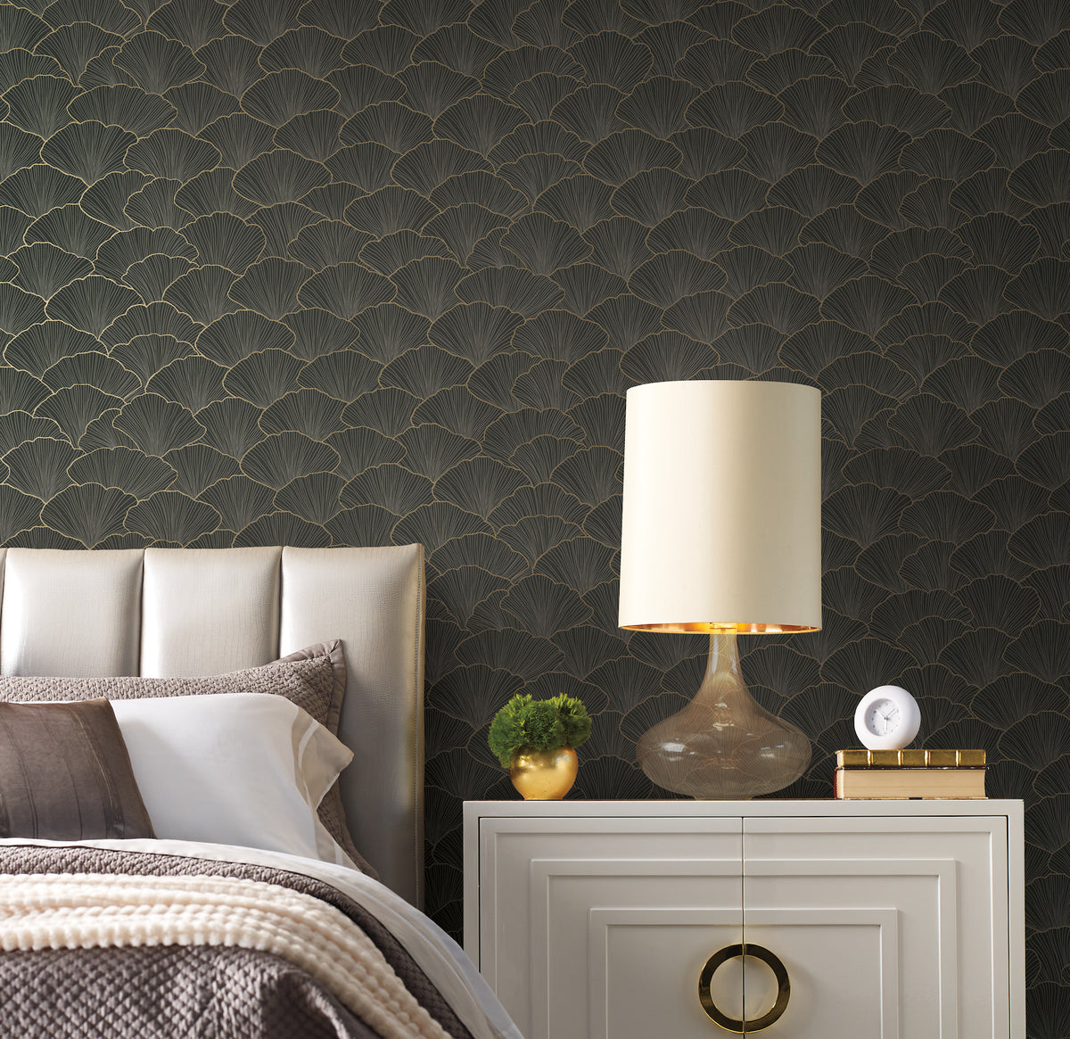 Candice Olson Luminous Gingko Wallpaper featuring a dark background with a repeating gold-outlined fan-shaped leaf pattern behind a bedroom nightstand and headboard.