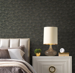Candice Olson Luminous Gingko Wallpaper featuring a dark background with a repeating gold-outlined fan-shaped leaf pattern behind a bedroom nightstand and headboard.