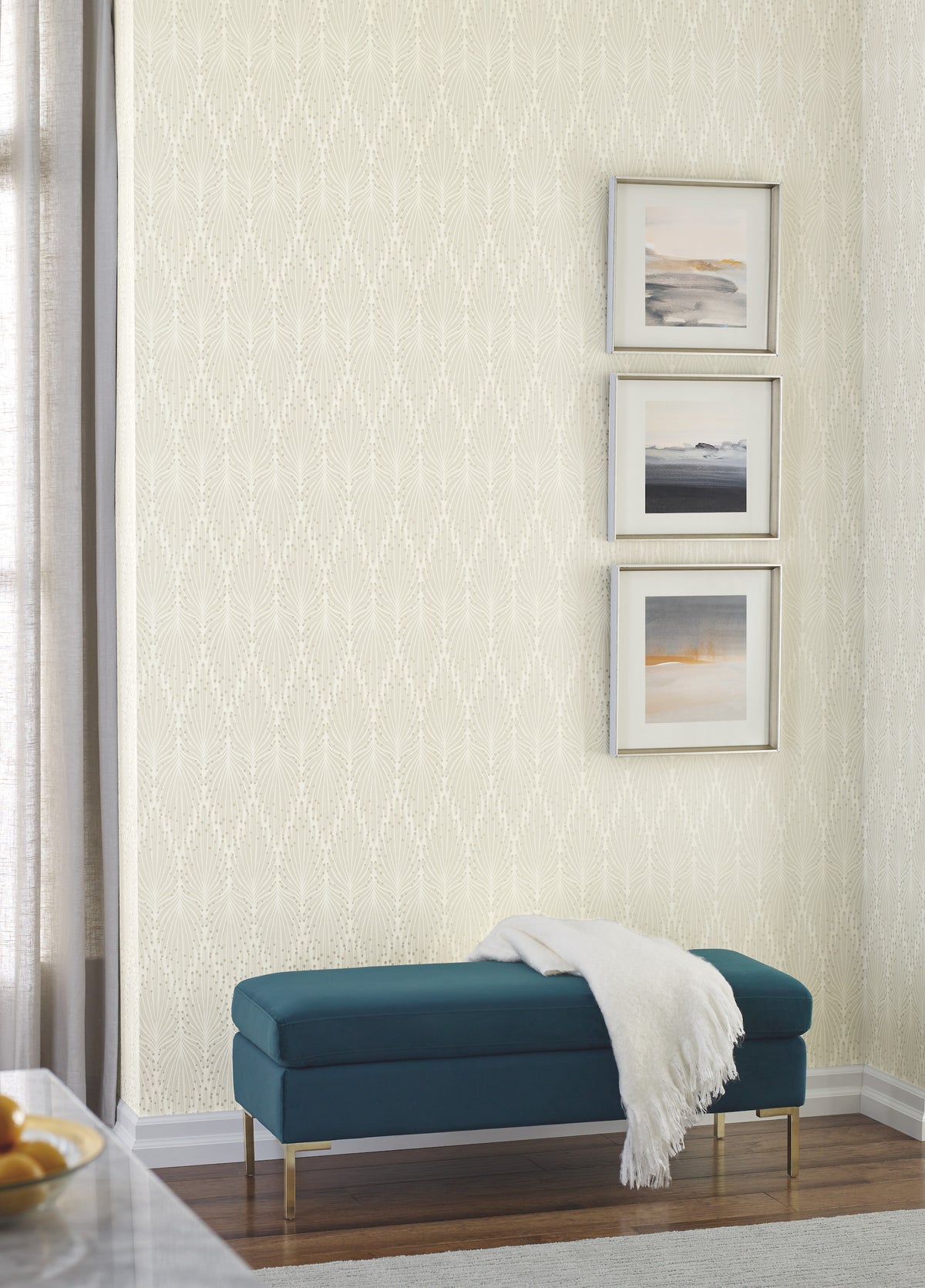 A teal upholstered bench with a white throw blanket sits against a wall covered in Candice Olson Café Society Wallpaper by York Wallcoverings, featuring a light-colored, cream-toned vertical fan-like pattern.