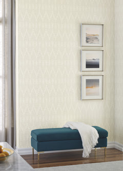 A teal upholstered bench with a white throw blanket sits against a wall covered in Candice Olson Café Society Wallpaper by York Wallcoverings, featuring a light-colored, cream-toned vertical fan-like pattern.