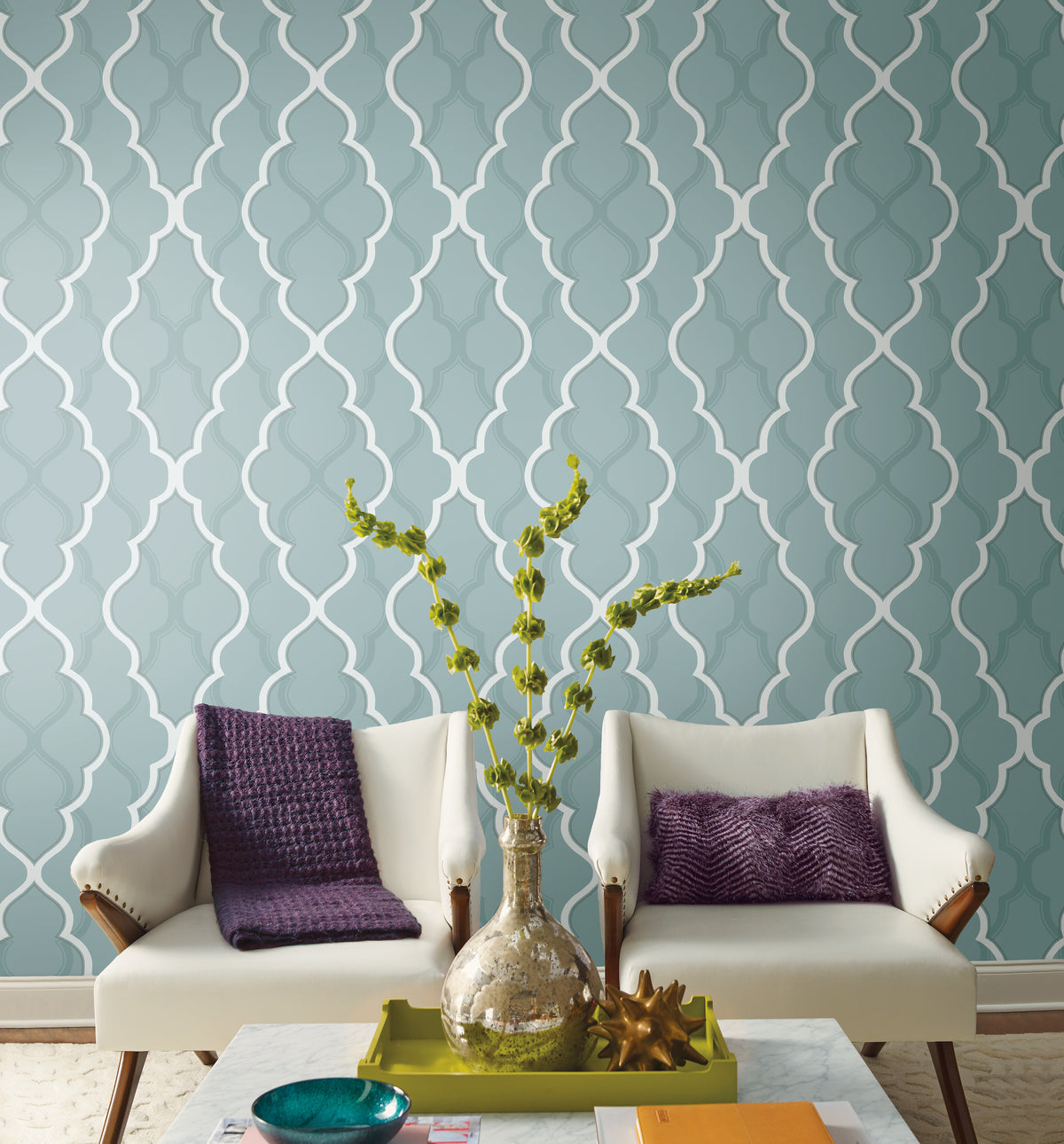 Two white armchairs face a table in front of a wall covered in Candice Olson Double Damask Wallpaper, featuring a teal background with a white, repeating trellis pattern.