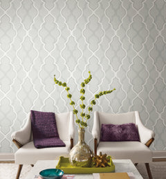 Two cream-colored armchairs with purple pillows positioned in front of Candice Olson Double Damask Wallpaper by York Wallcoverings, featuring a repeating light gray and white quatrefoil pattern.