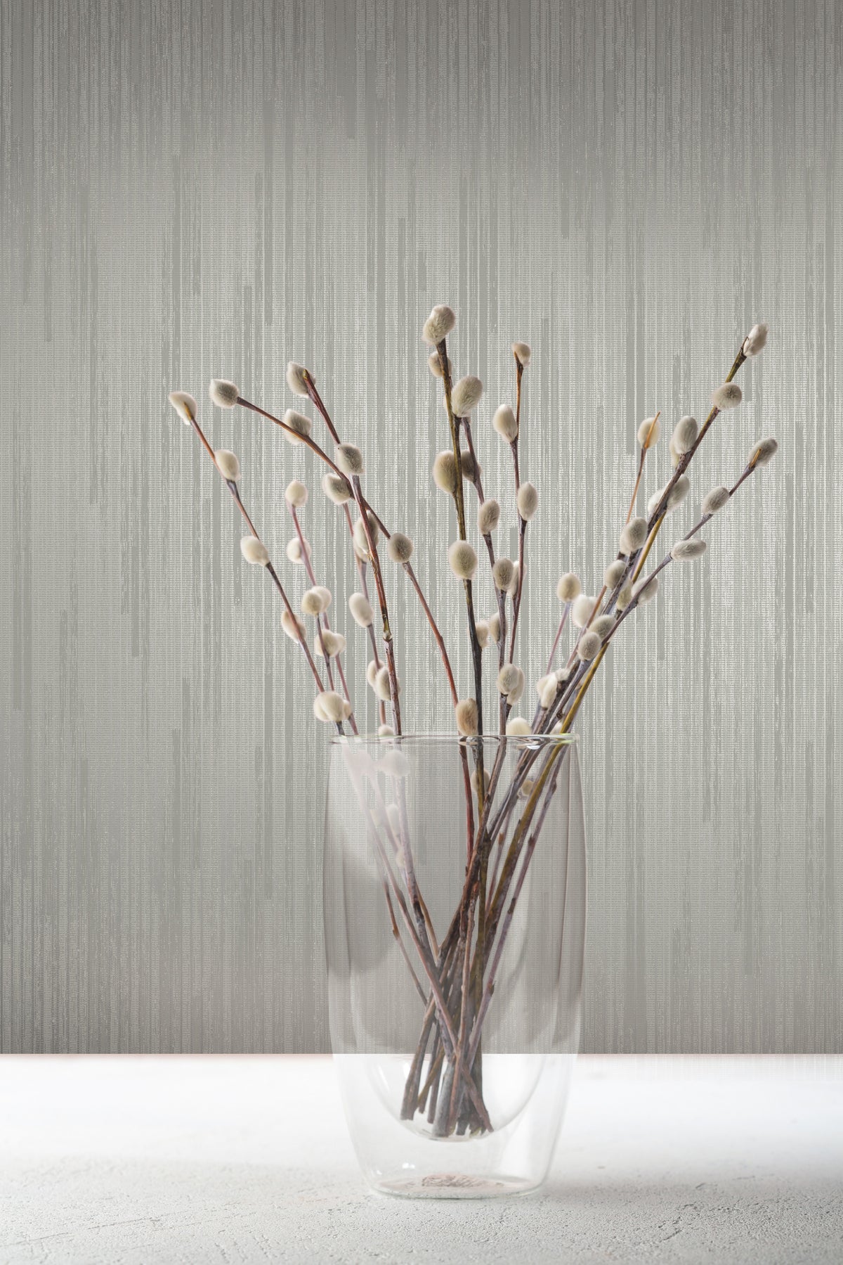 A glass vase filled with pussy willow branches stands against grey Candice Olson Bargello Wallpaper by York Wallcoverings.
