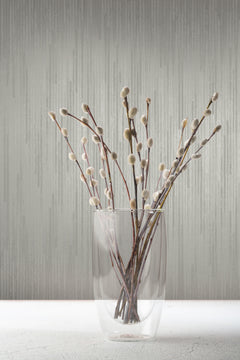 A glass vase filled with pussy willow branches stands against grey Candice Olson Bargello Wallpaper by York Wallcoverings.